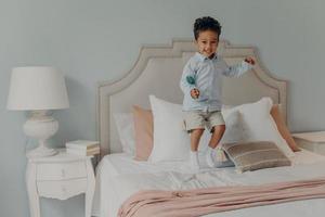 Energetic afro american kid jumping with lollipop on bed mattress photo