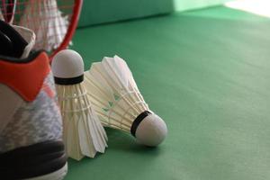 Badminton sport equipments on green floor of badminton court shuttlecocks, rackets, shoes, selective focus on shuttlecocks, badminton sport playing lover around the world concept. photo