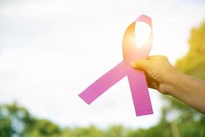 cinta rosa sosteniendo en la mano a una mujer joven con antecedentes borrosos, concepto para apoyar la lucha contra el cáncer de mama en mujeres de todo el mundo. foto