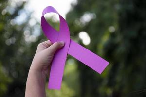 Pink ribbon holding in hand of young female with blurred background, concept for supporting fighting breast cancer in woman around the world. photo