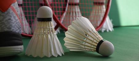 Badminton sport equipments on green floor of badminton court shuttlecocks, rackets, shoes, selective focus on shuttlecocks, badminton sport playing lover around the world concept. photo