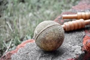 antiguos equipos deportivos de cricket de entrenamiento en suelo oscuro, pelota de cuero, wickets, casco y bate de madera, enfoque suave y selectivo, concepto tradicional de amantes del deporte de cricket en todo el mundo. foto