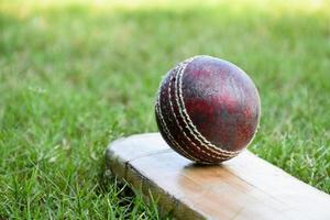 primer plano de equipos deportivos de cricket antiguos en suelo verde, pelota de cuero antigua, bate de madera, enfoque suave y selectivo, concepto tradicional de los amantes del deporte de cricket en todo el mundo. foto