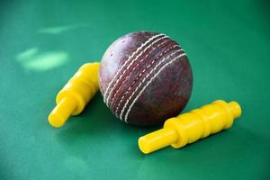 primer plano de equipos deportivos de cricket antiguos en suelo verde, pelota de cuero antigua y portillos de plástico amarillo, enfoque suave y selectivo, concepto tradicional de los amantes del deporte de cricket en todo el mundo. foto