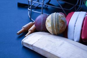 Old training cricket sport equipments on dark floor, leather ball, wickets, helmet and wooden bat, soft and selective focus, traditional cricket sport lovers around the world concept. photo