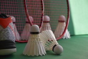 Badminton sport equipments on green floor of badminton court shuttlecocks, rackets, shoes, selective focus on shuttlecocks, badminton sport playing lover around the world concept. photo