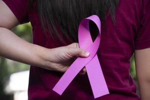 cinta rosa sosteniendo en la mano a una mujer joven con antecedentes borrosos, concepto para apoyar la lucha contra el cáncer de mama en mujeres de todo el mundo. foto