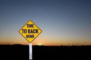 Yellow label traffic sign on pole which has texts 'Time to back home'' with blurred sunset background, concept for informing driver to drive vehicle straight home to stay with family around the world. photo