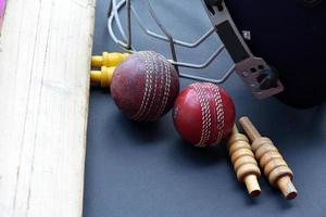 Old training cricket sport equipments on dark floor, leather ball, wickets, helmet and wooden bat, soft and selective focus, traditional cricket sport lovers around the world concept. photo