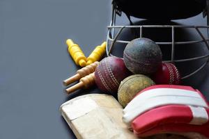 Old training cricket sport equipments on dark floor, leather ball, wickets, helmet and wooden bat, soft and selective focus, traditional cricket sport lovers around the world concept. photo