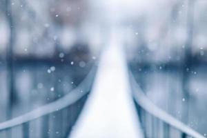 blurred photo of Pedestrian suspension bridge made of steel and wood across the river, winter