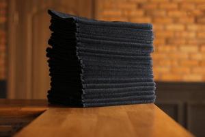 stacked black bathroom towels on a wooden table and brick wall background. spa salon, barbershop. photo