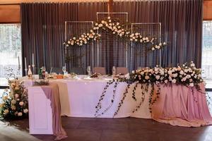 Wedding. Banquet. The festive table for bride, groom and guests, decorated with a composition of white and pink flowers and greenery, there are candles, served with crockery in restorane photo