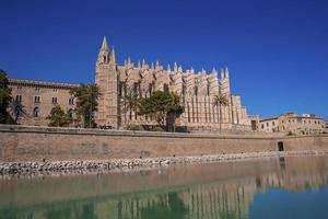 Medieval La Seu Cathedral reflecting in canal water against clear blue sky photo