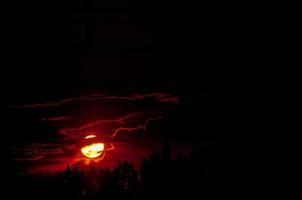 Red sun setting through the clouds in the woods photo