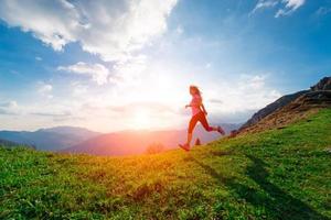atleta femenina entrena corriendo en los prados de la ladera al atardecer foto