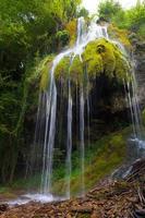 Small waterfall of water between the moss above a cave photo