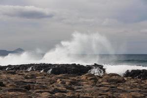 Las olas turbulentas del océano con espuma blanca golpean las piedras costeras. foto