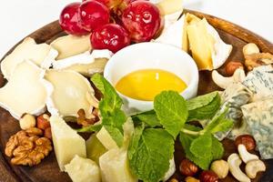 Various types of cheese with honey, nuts and grapes on plate, isolated on white photo