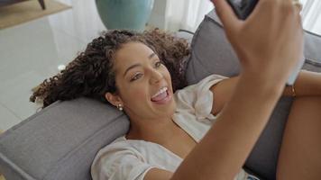 Happy Latin lady relax at home alone sit on room pose share good news at social media via cellphone. photo