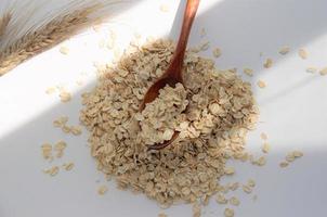 oat flakes raw on a wooden spoon on a white background, close-up photo