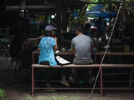 Chiang Mai, Thailand, 2021 - Asian men and women have breakfast in the Saturday flea market, shot from behind. photo