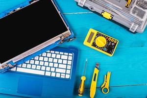 Wizard repairs laptop with tools and hands on the blue wooding table. top view photo