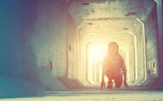 retroiluminación de un adolescente deprimido sentado dentro de un túnel sucio foto