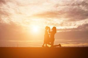 a silhouette of a happy young girl child the arms of his loving mother for a hug, in front of the sunset in the sky on a summer day. photo