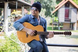 joven hipster tocando guitarra para relajarse en sus vacaciones, disfrutar con aire fresco y natural. foto