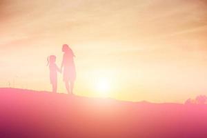 Mother encouraged her daughter out of the shadows at sunset. photo