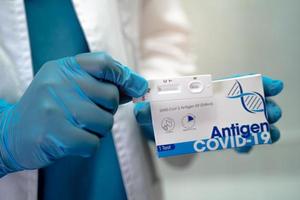 Asian doctor in PPE suit holding Saliva Antigen Test Kit for check Covid-19 coronavirus in hospital. photo