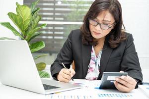 Asian accountant working and analyzing financial reports project accounting with chart graph and calculator in modern office, finance and business concept. photo