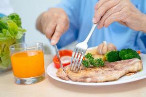 Asian senior or elderly old lady woman patient eating breakfast and vegetable healthy food with hope and happy while sitting and hungry on bed in hospital. photo