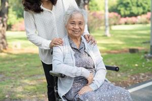 Caregiver help and care Asian senior or elderly old lady woman patient sitting and happy on wheelchair in park, healthy strong medical concept. photo