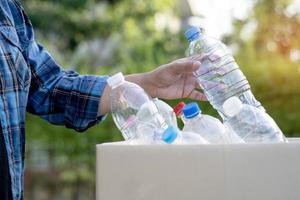 Asian woman volunteer carry water plastic bottles into garbage box trash in park, recycle waste environment ecology concept. photo