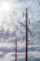 Two high-voltage towers with a concrete base against a cloudy sky. photo