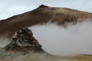 Volcanic fumarole emitting gas and sulfur emanating from a pile of rocks on brown ground photo