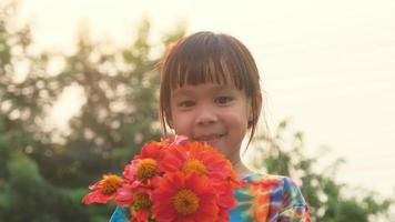 portret van een schattig klein meisje met een lenteboeket op een zonnige zomeravond. lachend meisje met een boeket verse oranje bloemen in haar hand. video