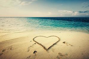 forma de corazón dibujada en una arena a la orilla del mar.