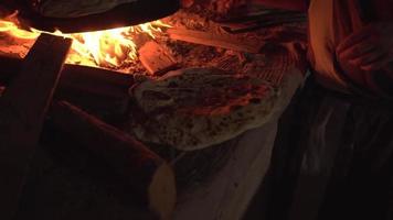pan recién horneado colocado en primer plano mientras se arroja más masa sobre piedra en el horno de fuego video