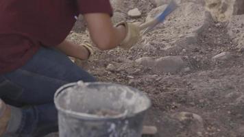 Erwachsener verwendet Spitzhacke auf Felsoberfläche, Fokusverlagerung auf Eimer im Vordergrund video
