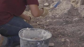 Adult Uses Pick Axe on Rock Surface, Focus Shift to Bucket in Foreground video