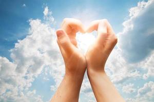 Man and woman hands make a heart on blue sunny sky. Love photo