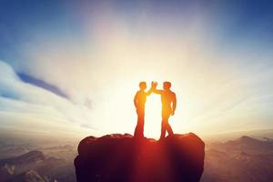 dos hombres, amigos chocan los cinco en la cima de las montañas. convenio foto