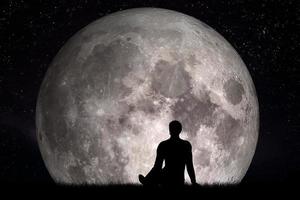 Man sitting alone on grass and looking on moon. Imagine the future concept. photo