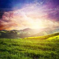 Fairtytale landscape with green grass, mountains, sunset fantastic sky. photo