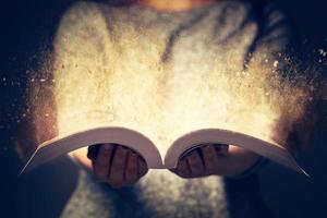 Woman holding an open book bursting with light. photo
