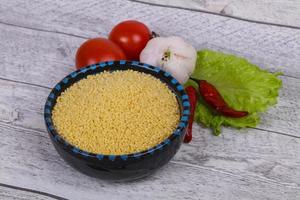 cuscús crudo en el bol servido con hojas de ensalada, tomate y pimiento foto