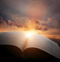 Open old book, light from sunset sky, heaven. Education, religion concept photo